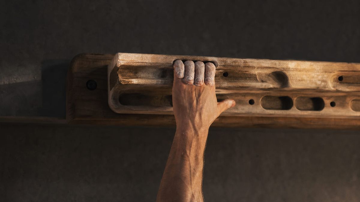 Chalked fingers on a wooden hangboard edge.